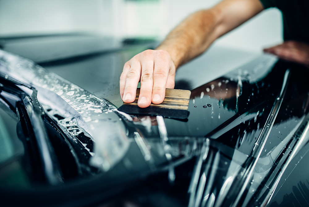 Specialist with squeegee installing Paint Protection film on a car.